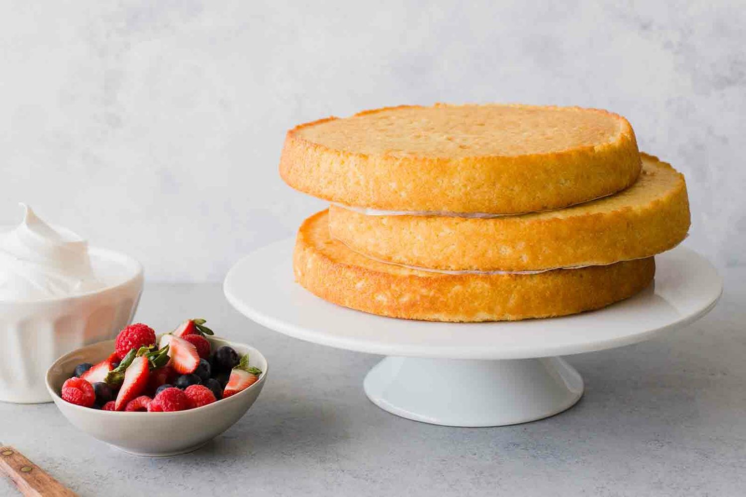 Une pile de couches de gâteau sur un plat à gâteau avec des baies et de la crème fouettée à côté