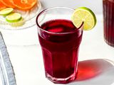 Agua de Jamaica (Hibiscus Tea) Served with Ice and a Lime Slice Next to a Small Plate of Sliced Oranges and Limes and a Pitcher with More Jamaica