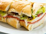 Side view of an italian sandwich on a platter that is cut into slices. Meat, cheese and toppings are layered on the sandwich.