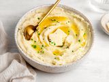 Vegan Mashed Potatoes in a Bowl Topped with Butter, Cracked Pepper, and Chives Next to a Saucer with More Butter