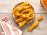 Twisted Cheese Straws on a Plate Next to a Drink and a Kitchen Towel. One Twisted Cheese Straw Is Broken in Half Next to the Plate.