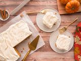 Pumpkin Snack Cake frosted with cream cheese is set on a table with two plates with pieces of cake to the right.