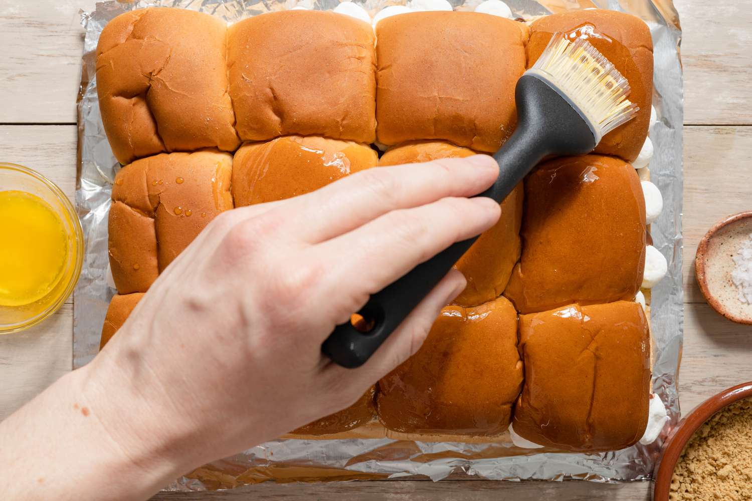 Sliders assemblés et le dessus des pains brossé avec du beurre, et à côté des sliders, un bol de miettes de biscuits Graham