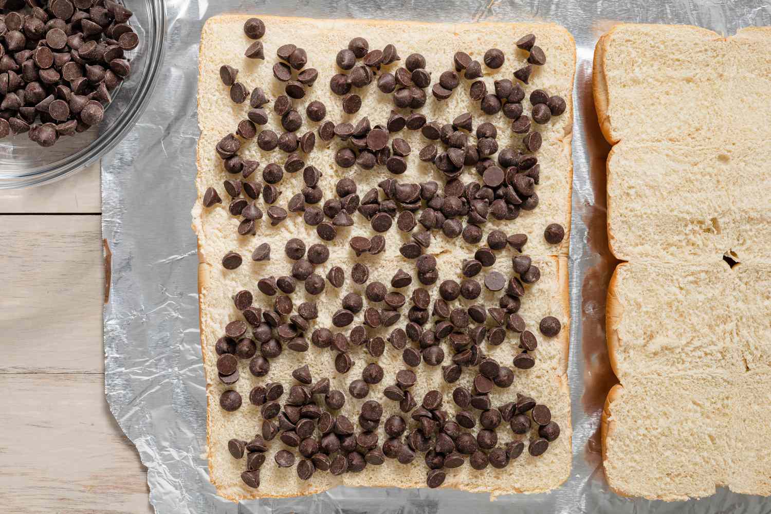 Pépites de chocolat sur l'une des tranches coupées. À gauche, un bol avec plus de pépites de chocolat et à droite, l'autre pain coupé pour la recette de slider s’mores grillés