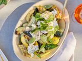 Bowl of Grilled Zucchini and Yellow Squash with Champagne Vinaigrette with a Spoon Surrounded by a Drink on a Table 