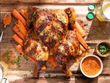 Smoked Spatchcock Chicken with Harissa Butter and Grilled Carrots on Cutting Board, Surrounded by Bowl of Harissa, Bowl of Herb, Kitchen Towel, and a Drink