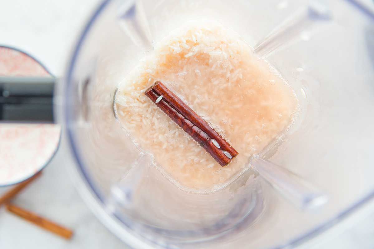 Overhead shot of inside of a blender with rice, liquid and a cinnamon stick for easy homemade horchata.