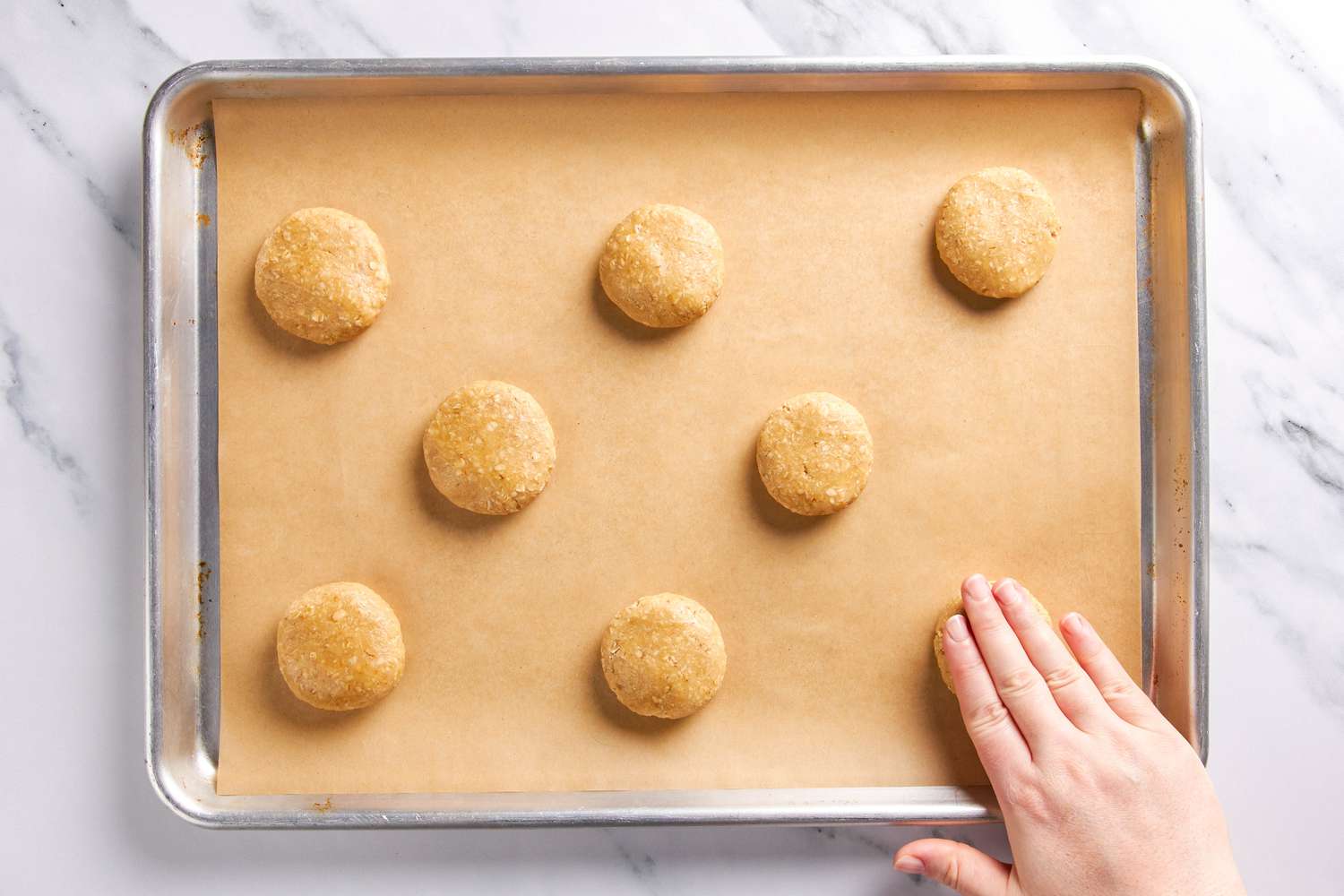 A hand slightly flattening the cookie dough balls on the lined baking sheet for yellowhammer cookie recipe