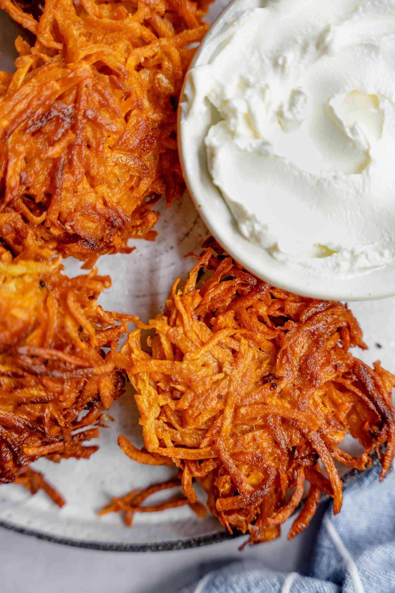 Assiette de latkes de patate douce servie avec un petit bol de crème aigre