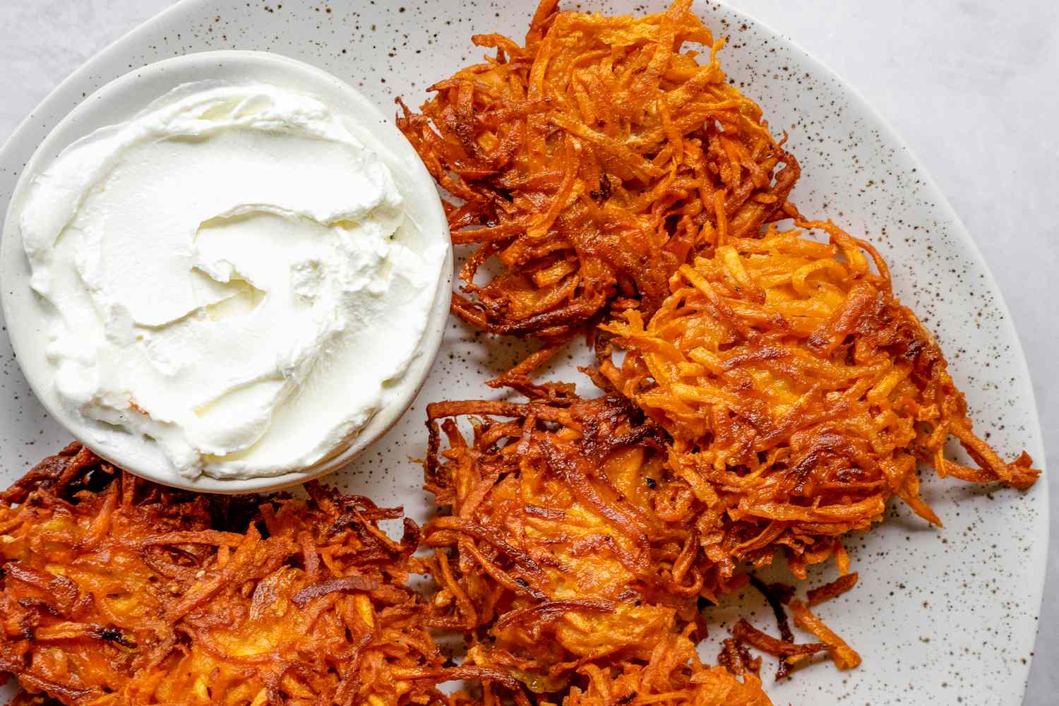 Assiette de latkes de patate douce servie avec un petit bol de crème aigre