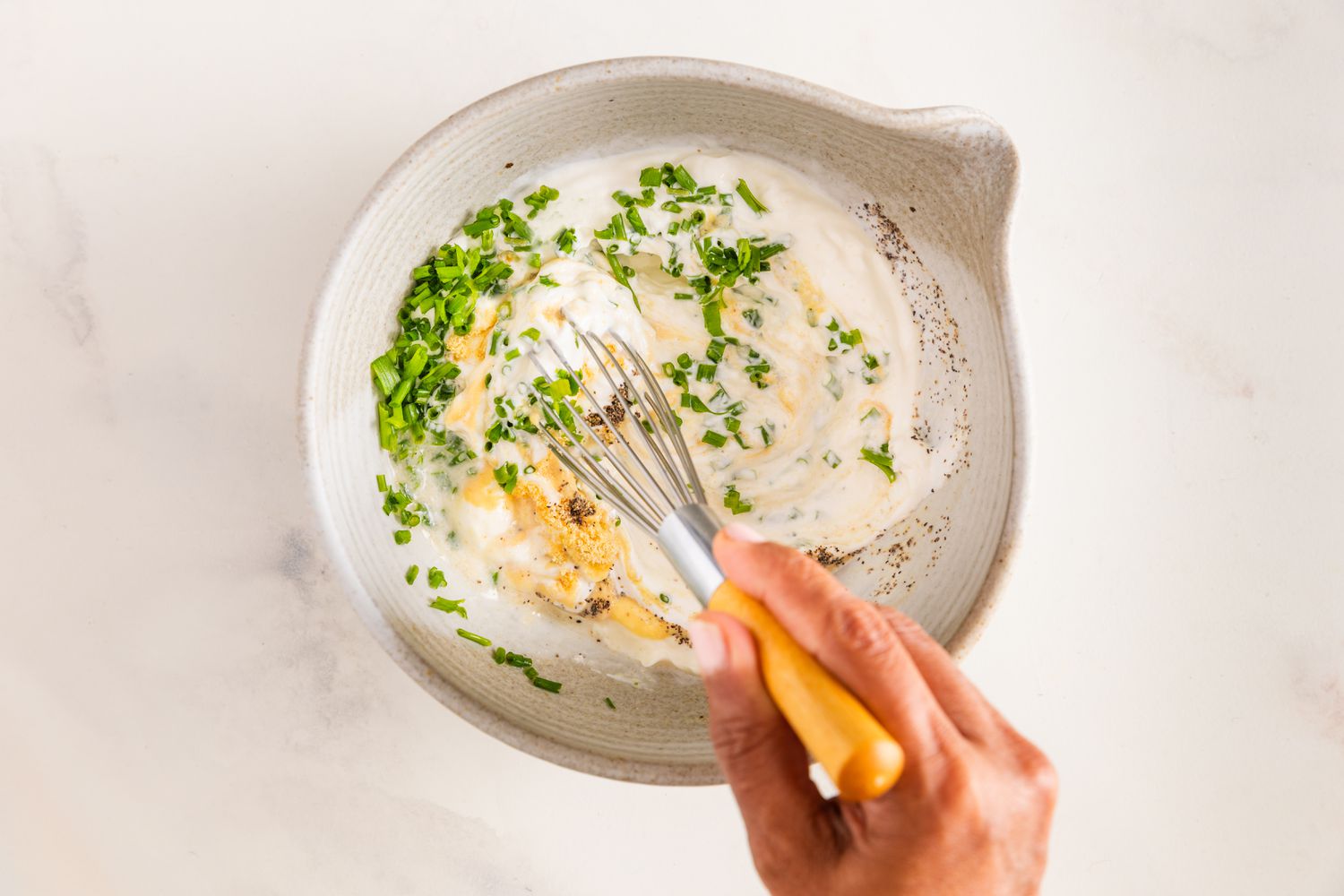 Fouet utilisé pour mélanger les ingrédients de la vinaigrette à la crème aigre et à l'oignon dans un bol pour la recette de salade de pommes de terres