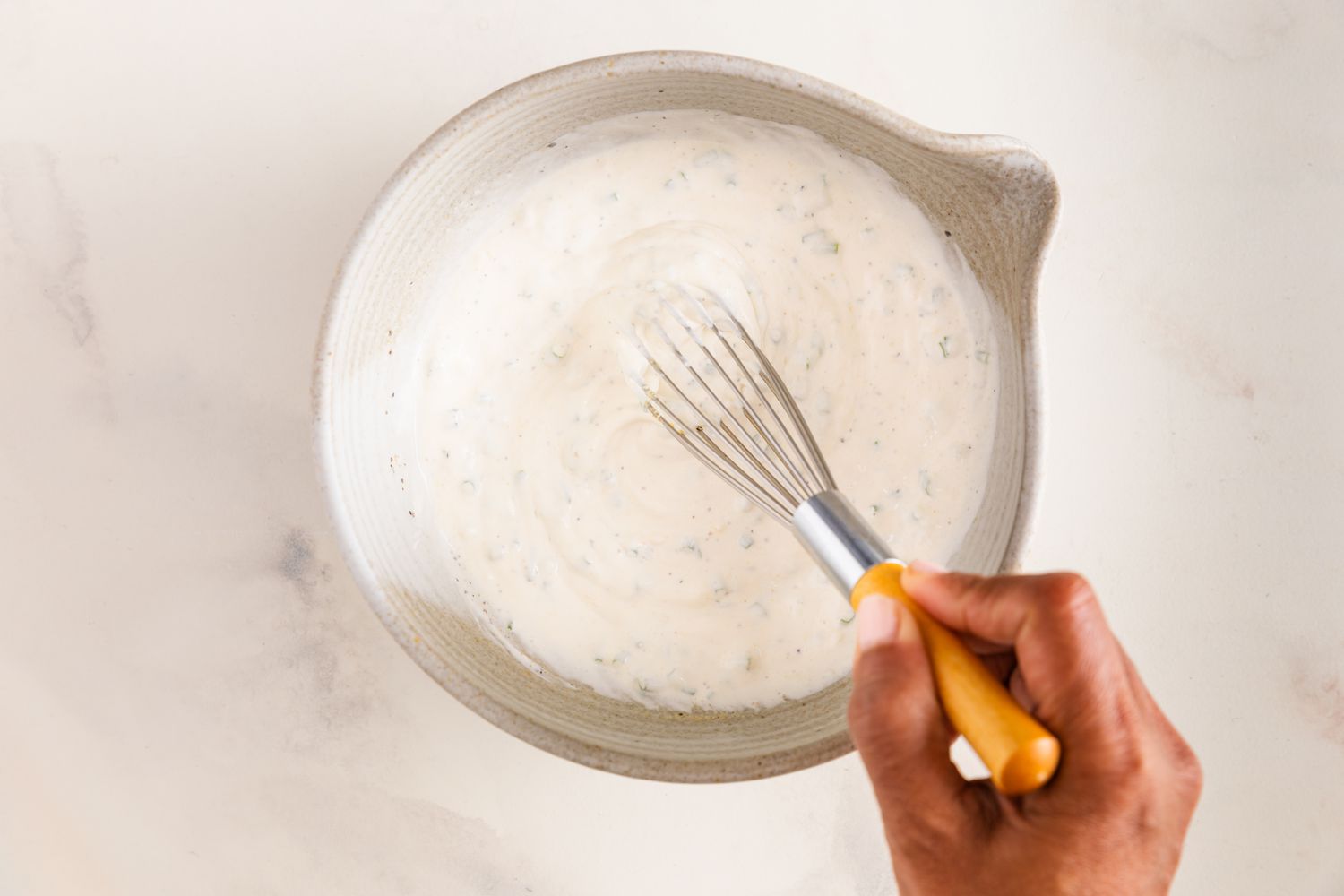 Ingrédients de la vinaigrette à la crème aigre et à l'oignon mélangés ensemble à l'aide d'un fouet dans un bol pour la recette de salade de pommes de terres