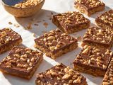 Oh Henry bars on a crinkled parchment paper with a bowl of crushed peanuts 