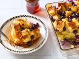 Plated serving of blueberry maple breakfast bake, drenched in maple syrup, alongside baking dish of the bake