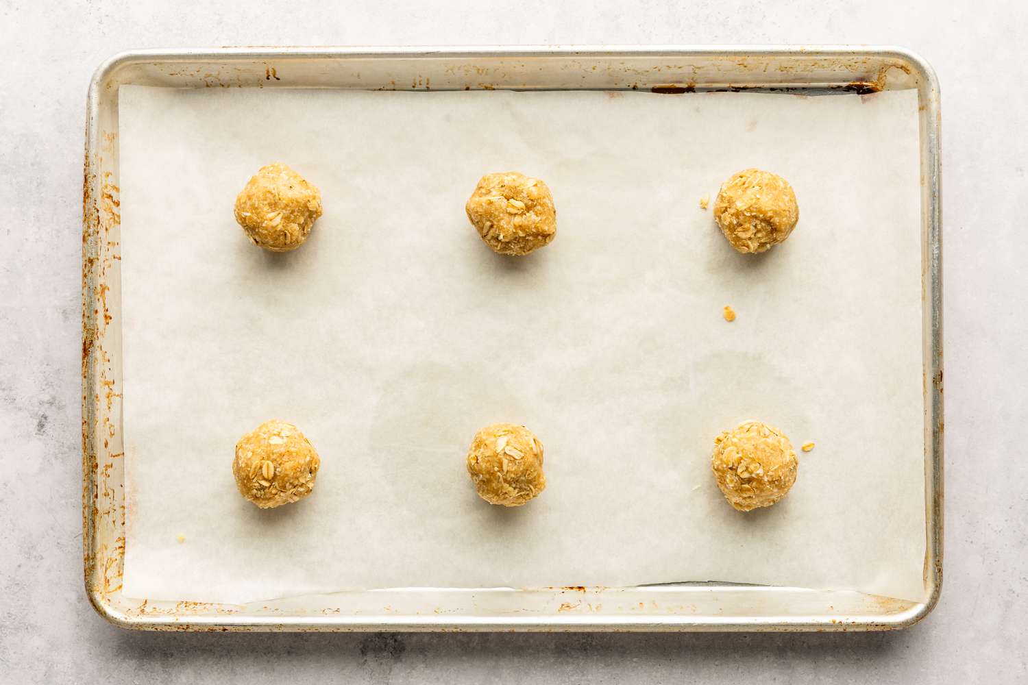 Six boules de pâte pour la recette des biscuits Anzac sur une plaque recouverte de papier sulfurisé