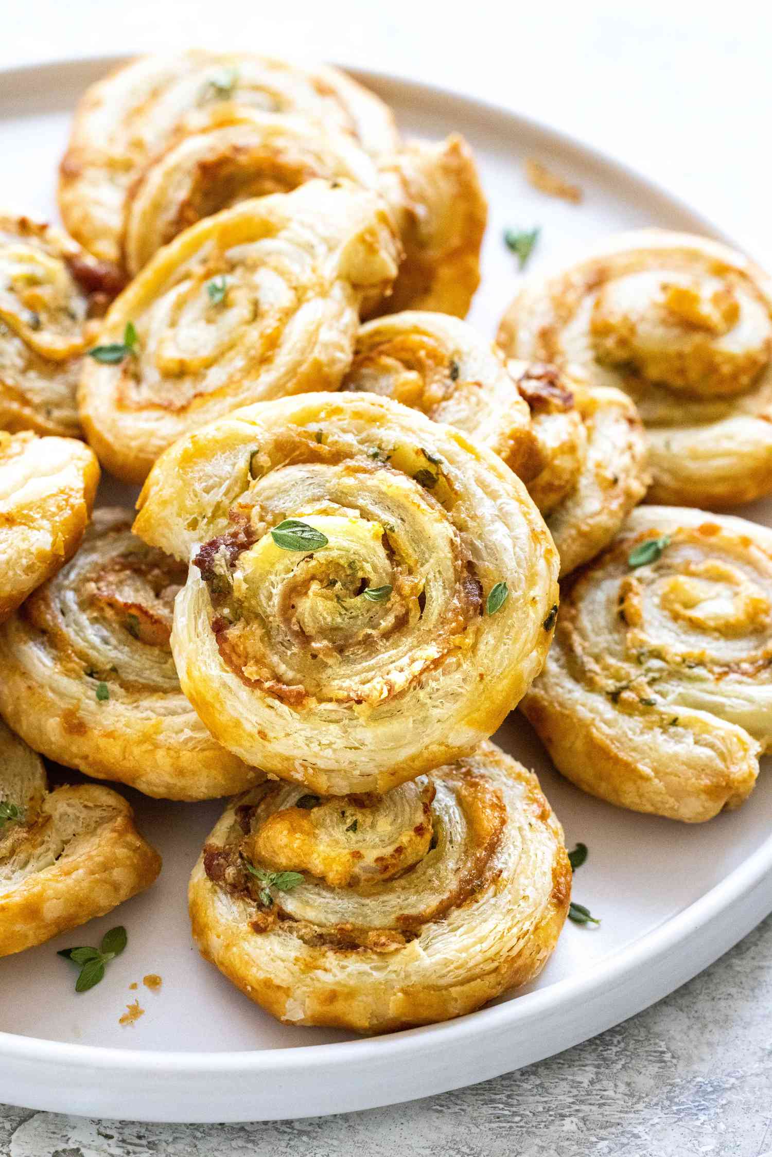 Close up of puff pastry pinwheels with prosciutto, Dijon mustard, and parmesan stacked on a platter.