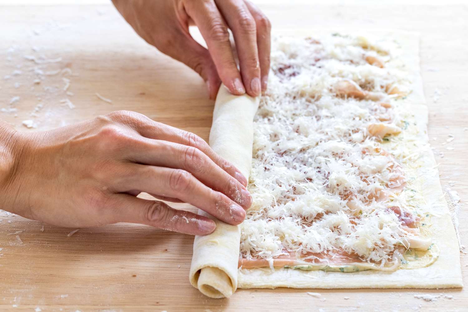 Rolling up the filled puff pastry to make savory pinwheels.