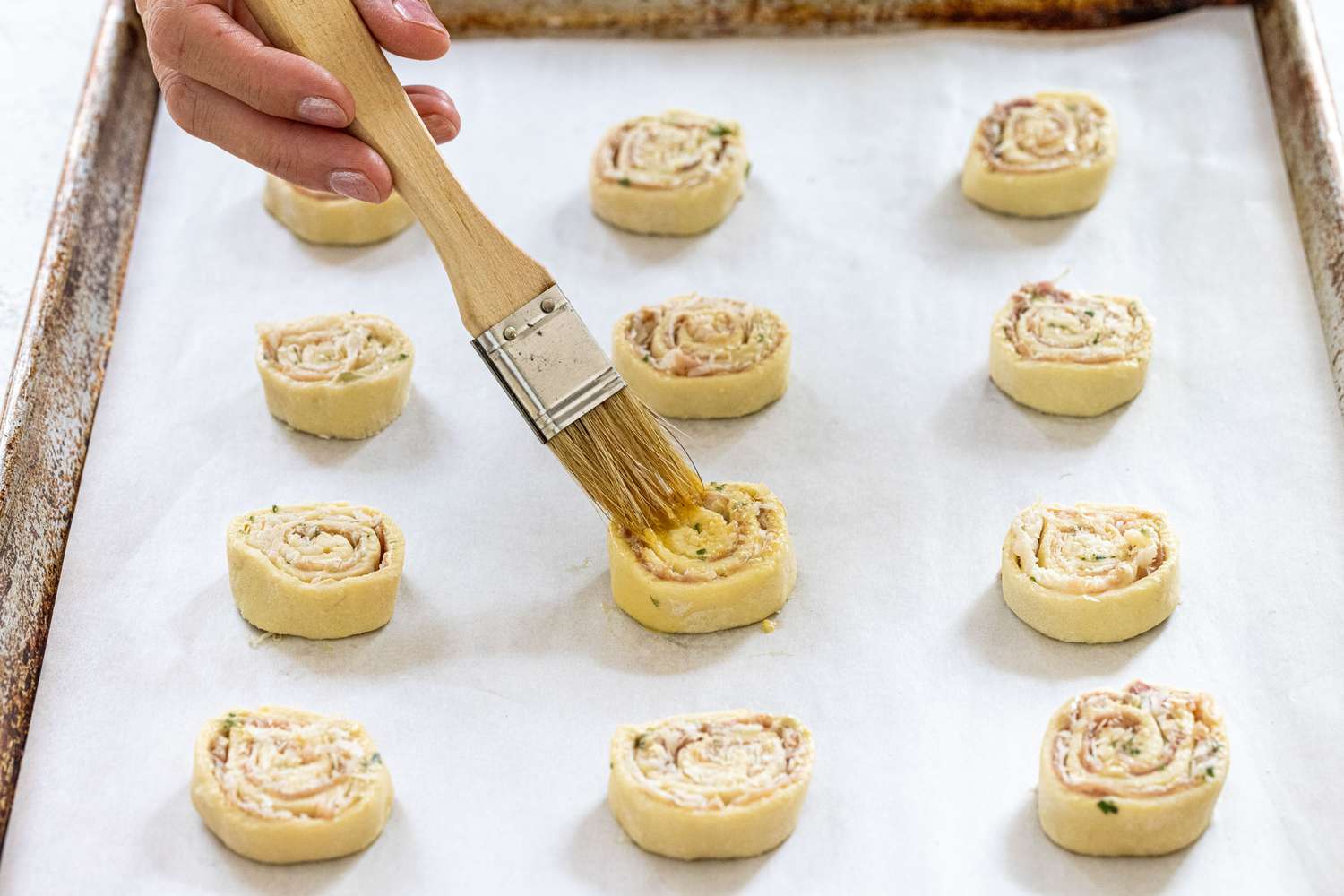 Brushing crispy prosciutto and parmesan pinwheels with egg wash before baking.