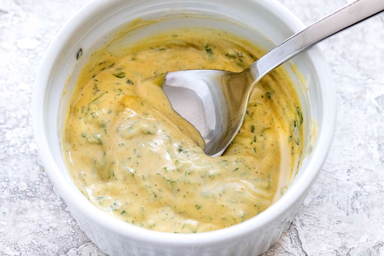 Mixing the herb spread for puff pastry pinwheels with prosciutto, Dijon mustard, and parmesan in a small bowl with a spoon.