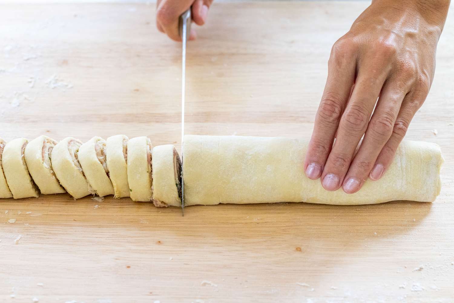 Slicing the rolled log with a knife to make crispy prosciutto and parmesan pinwheels.