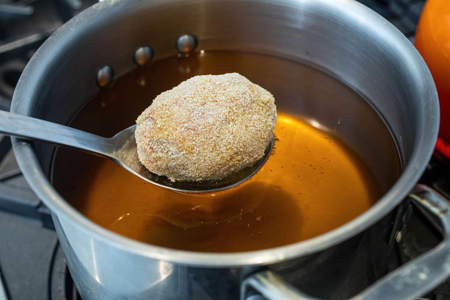 Abaisser les Scotch eggs dans l'huile avec une cuillère à fente.