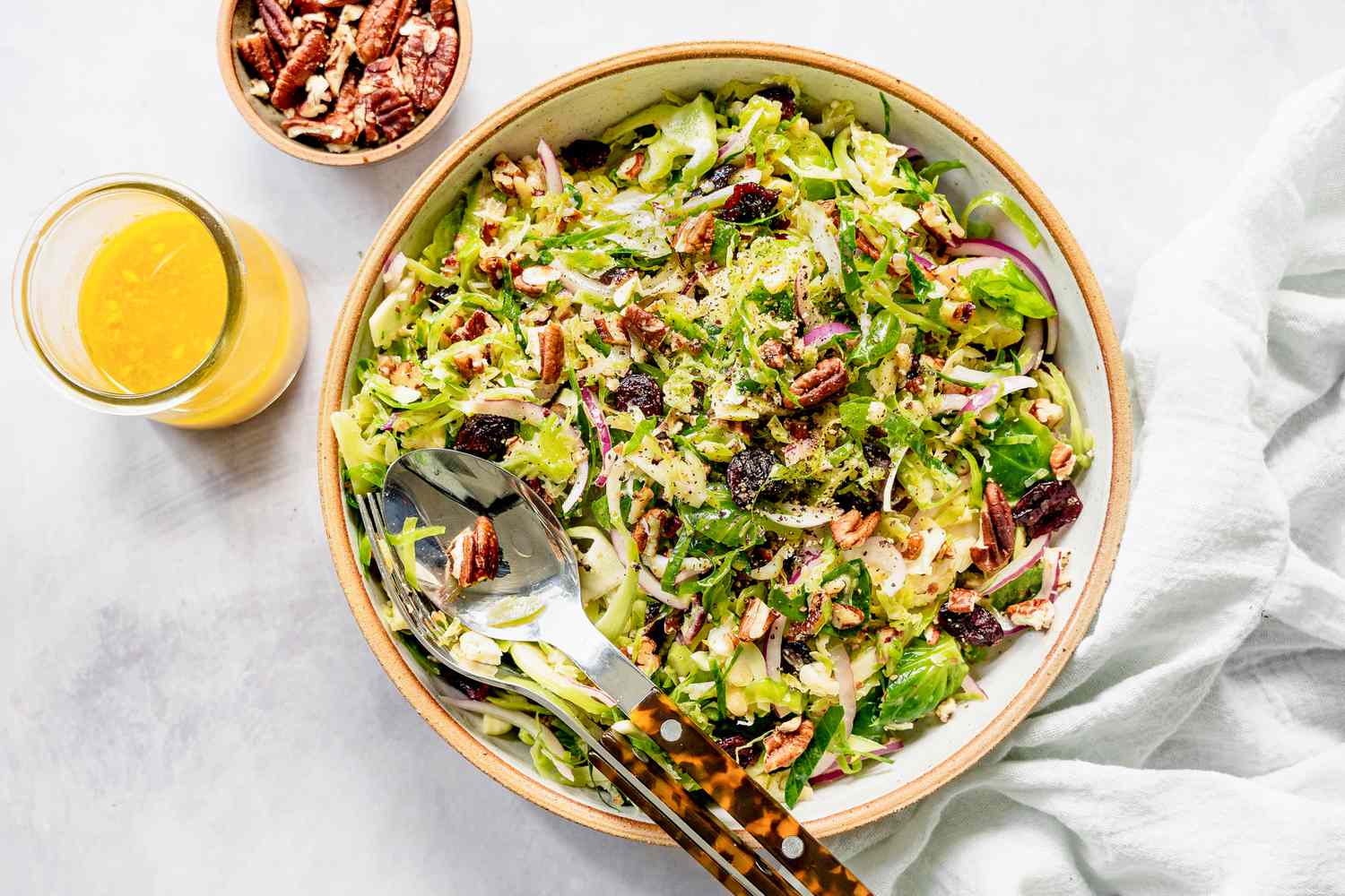 Brussel Sprout Cole Slaw in a Bowl Next to a Bowl of Dressing and Bowl of Pecans