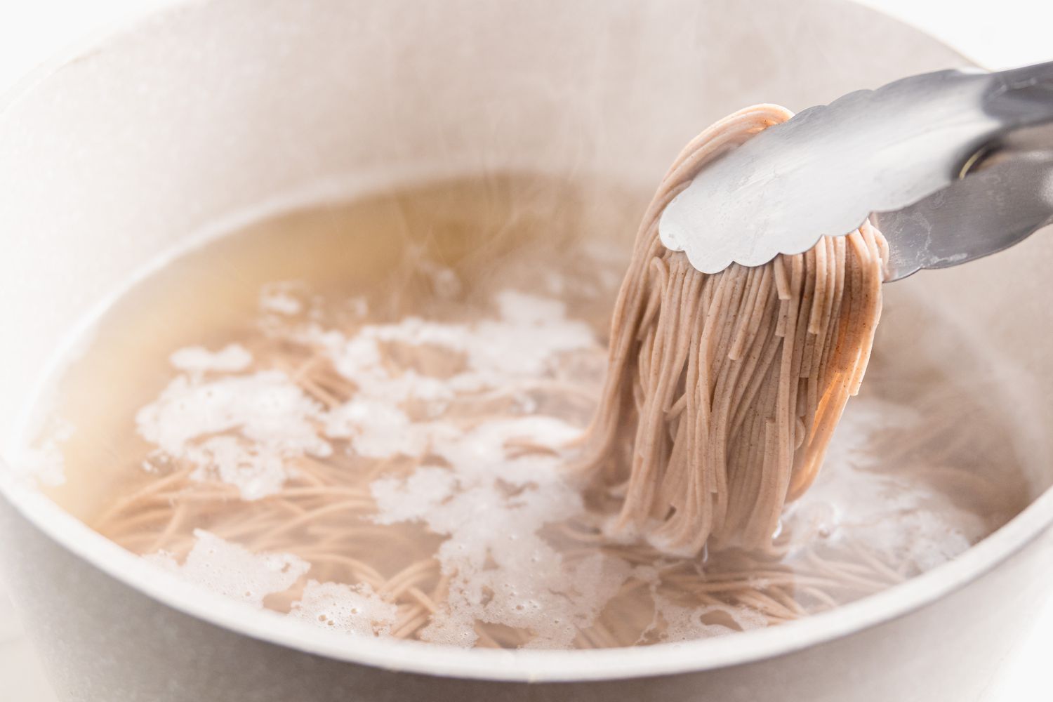 Nouilles soba cuites prises avec des pinces dans une casserole d'eau bouillante pour la recette des nouilles au sésame