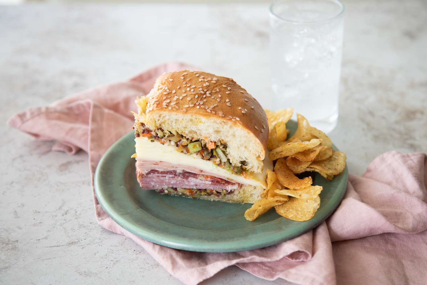 Classic Muffuletta on a Plate with Chips Next to a Glass of Soda