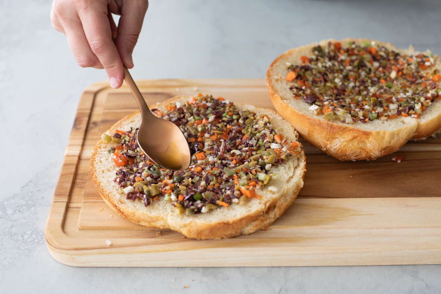 Minced Olive Mix Spooned onto Muffuletta Bread on Cutting Board