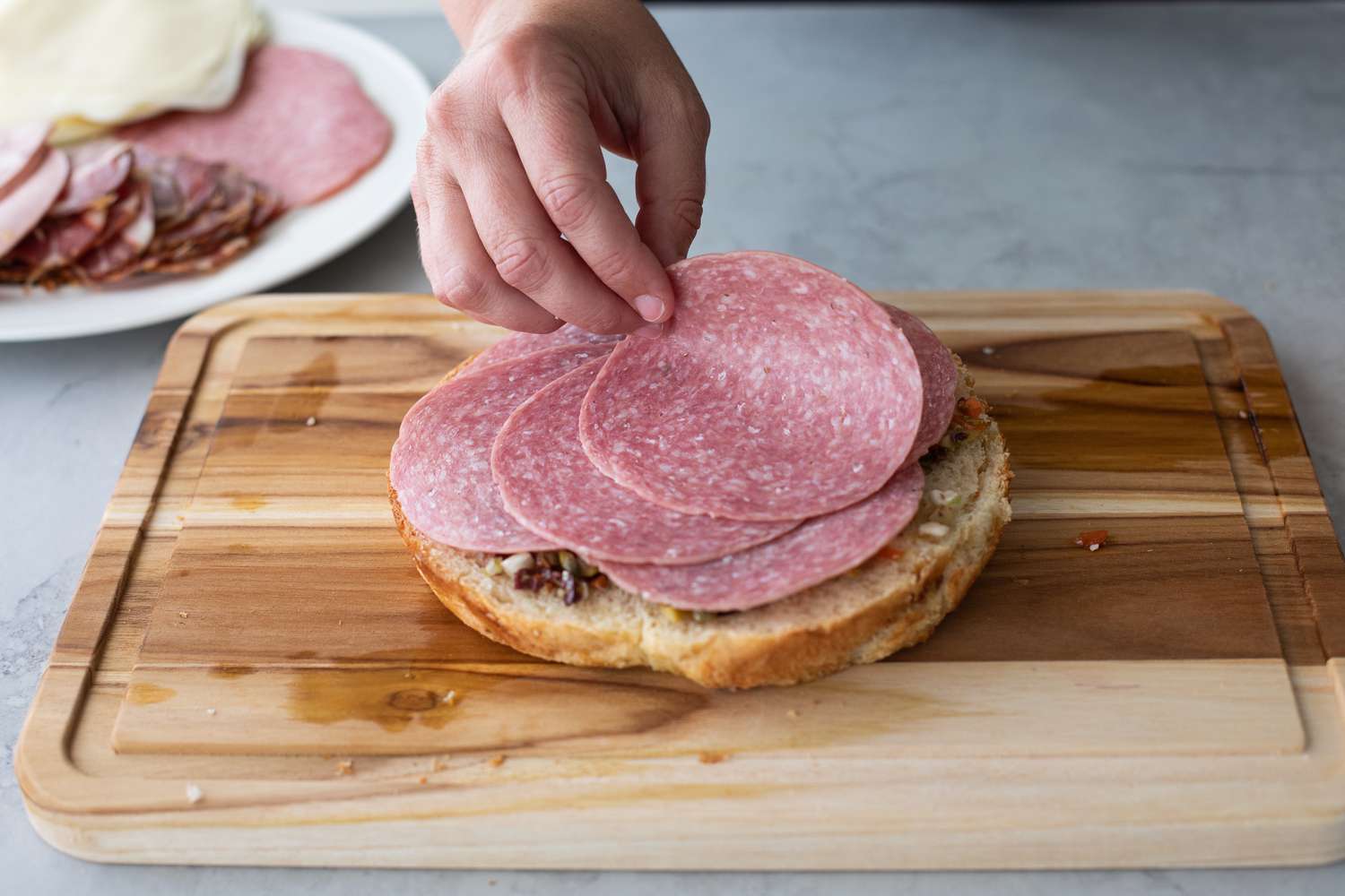 Salami Added to Classic Muffuletta on Cutting Board 