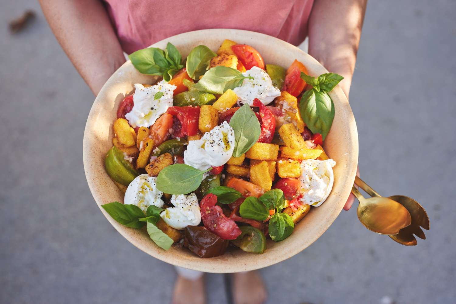 Quelqu'un tenant un Bol de Panzanella de Polenta Frite avec Tomate, Basilic et Burrata