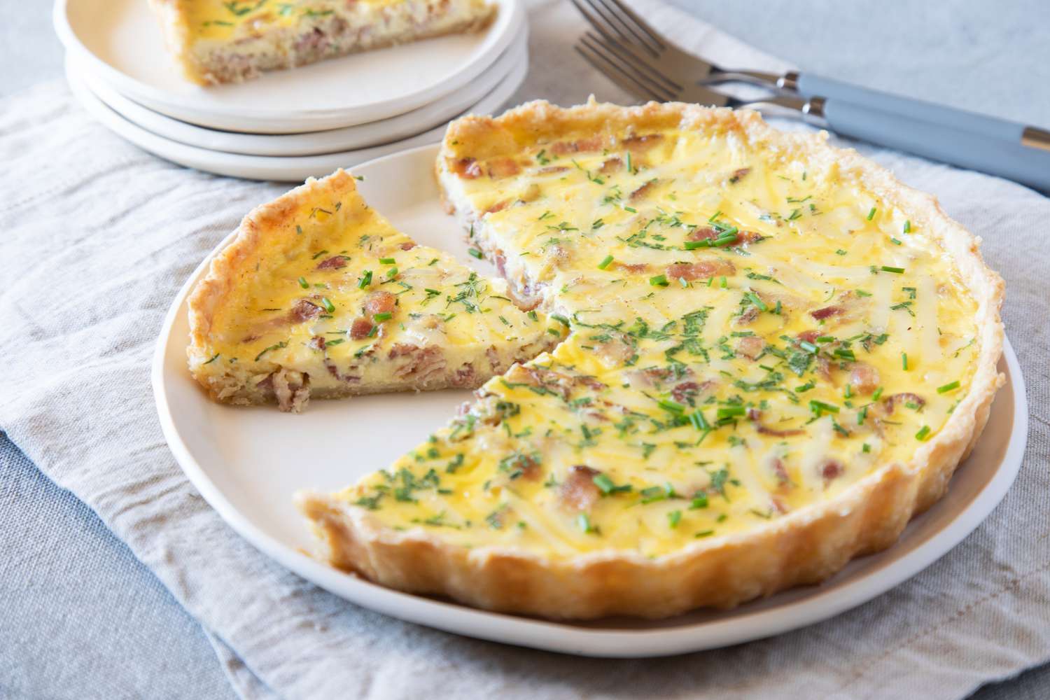 Quiche Lorraine avec une part placée sur une assiette derrière elle.