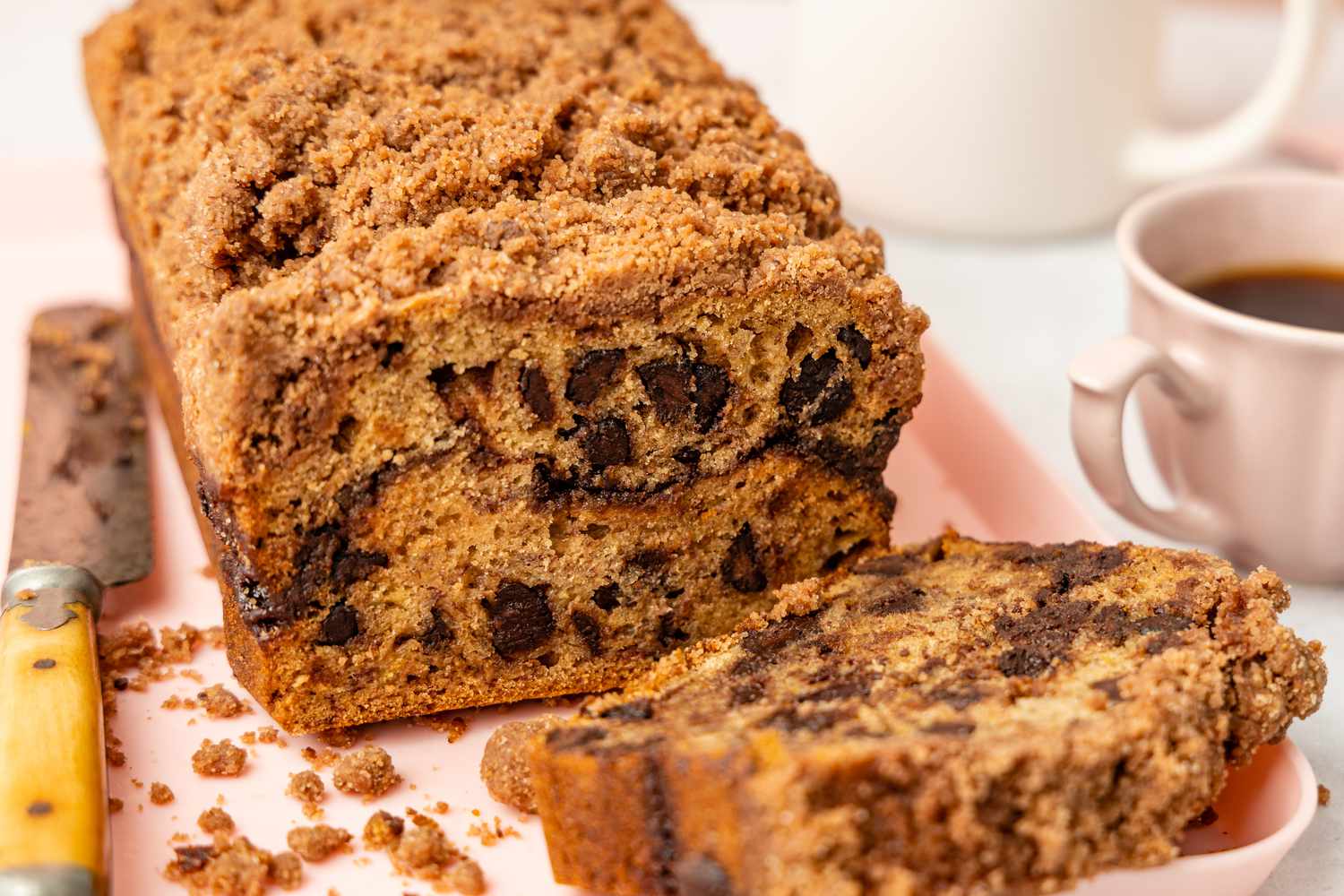 Pain de Gâteau avec Pépites de Chocolat et Banane sur une Assiette, et dans les Environs, un Couteau et une Tasse de Café