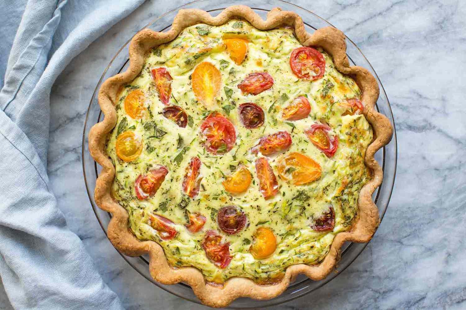 Quiche courgette tomate dans un plat à tarte en verre sur un comptoir en marbre.