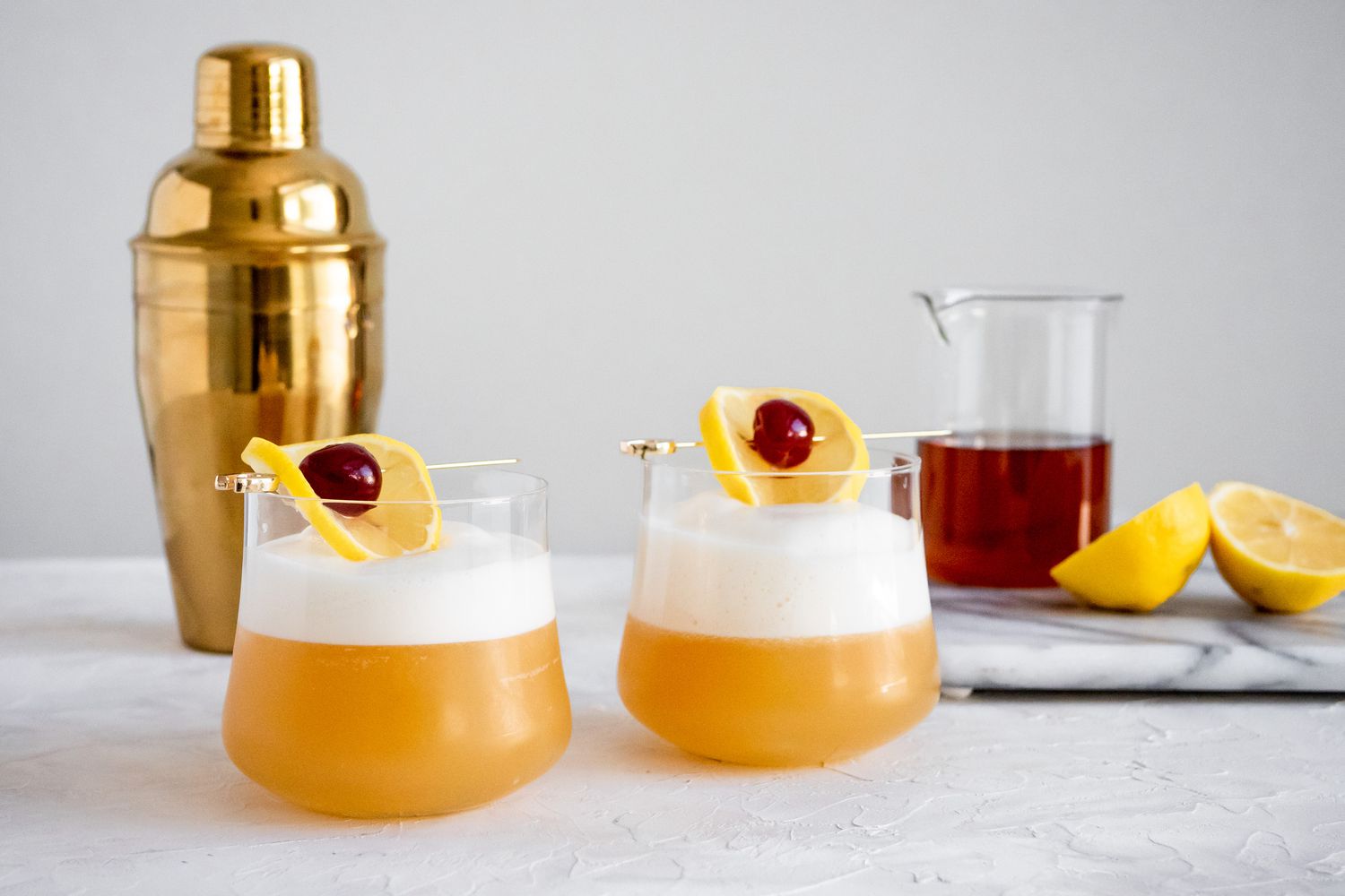 Deux Verres d'Amaretto Sour avec Ingrédients et Shaker à Cocktails en Arrière-plan