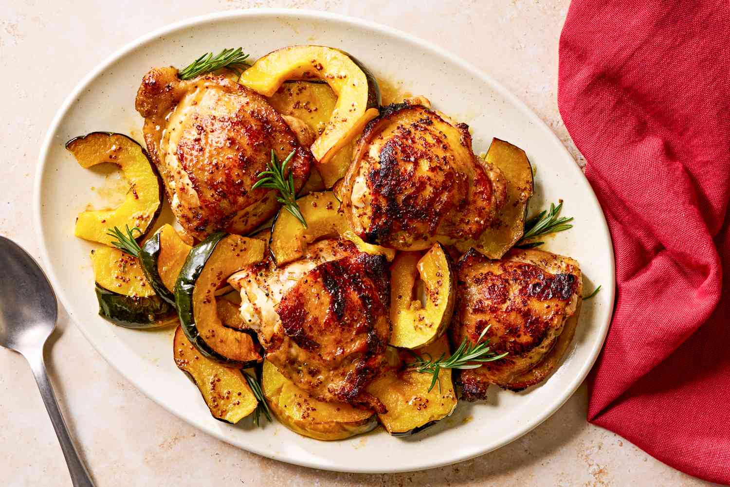 Vue de haut d'un plat blanc contenant du poulet glacé à l'érable et de la courge à côté d'une cuillère et d'une serviette en tissu rouge