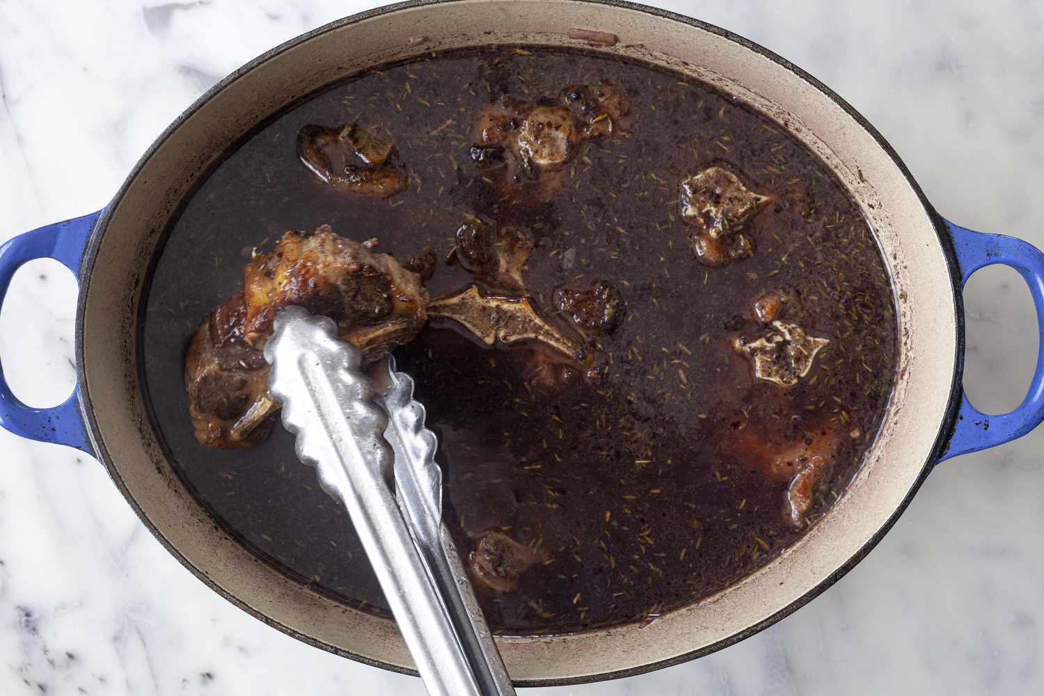 Queues de bœuf ajoutées au liquide de braisage dans une cocotte pour montrer comment cuisiner des queues de bœuf.