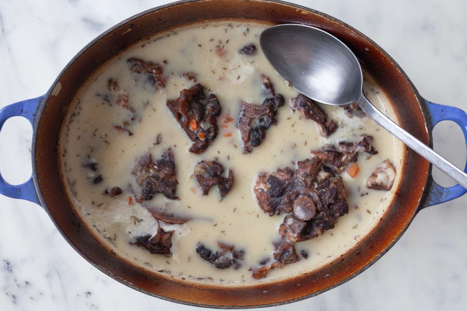 Retrait de la graisse d'une casserole de queues de bœuf glacées.