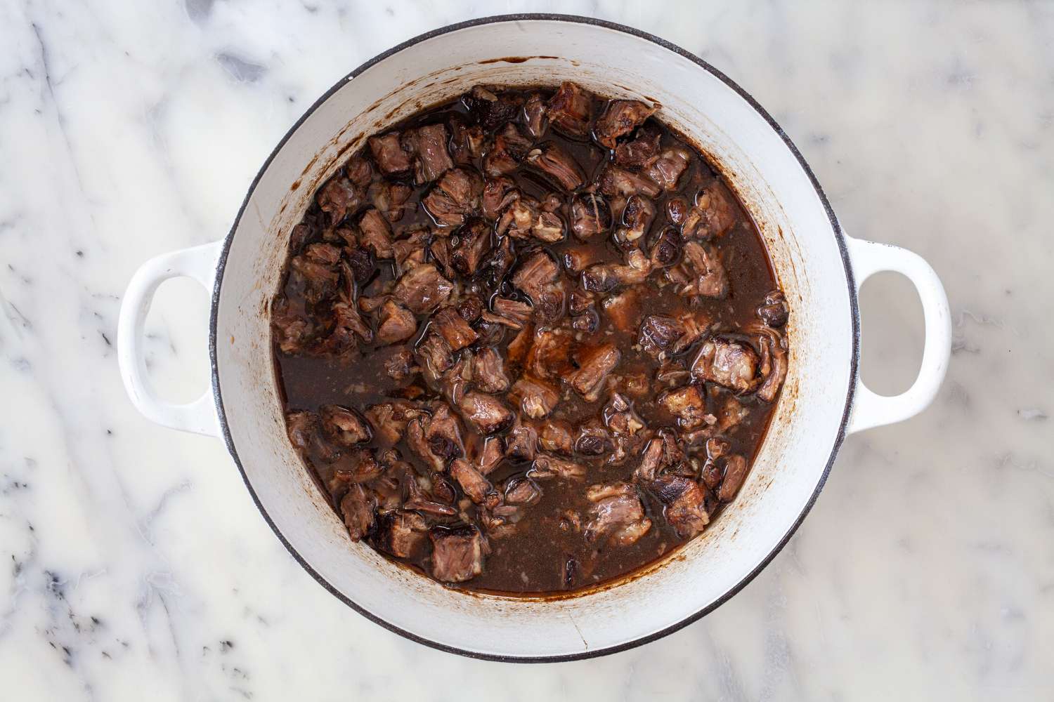 Viande ajoutée à nouveau dans le liquide de braisage pour montrer comment cuisiner des queues de bœuf.