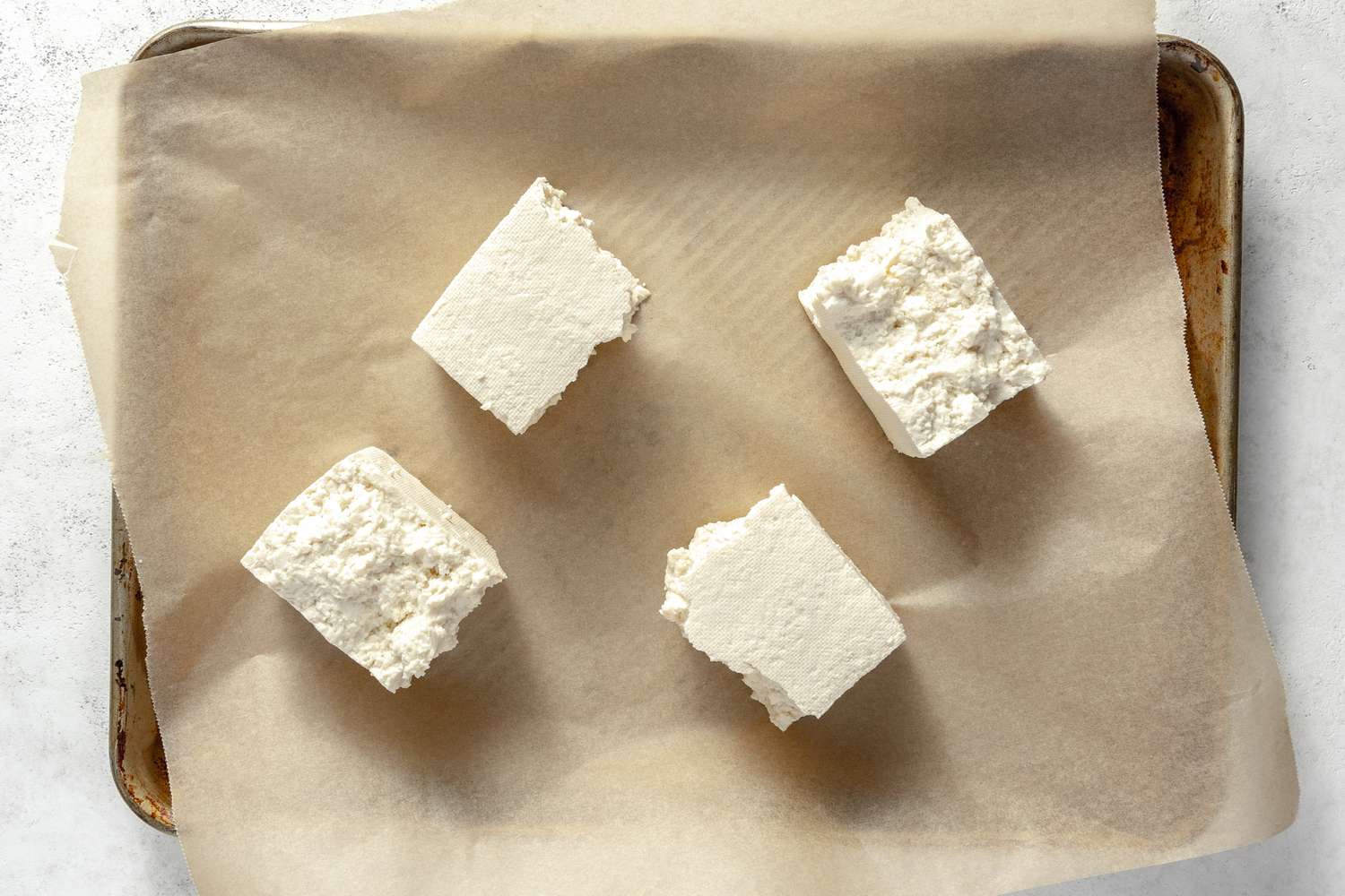 Tofu Block Broken into 4 Cubes on a Parchment Lined Baking Pan for Vegan Chicken Nuggets Recipe