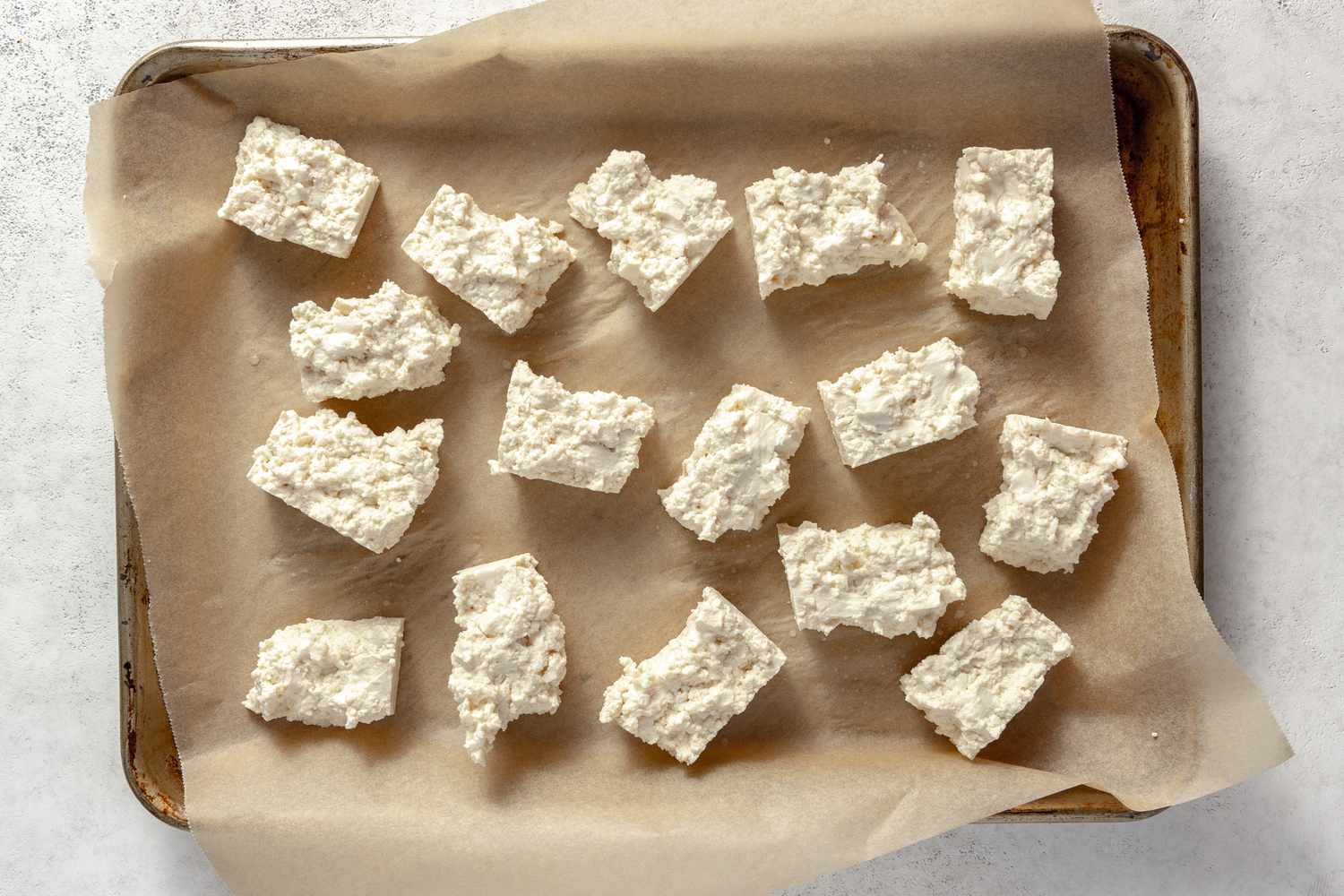 Tofu Block Broken into 16 Bite Size Pieces on a Parchment Lined Baking Pan for Vegan Chicken Nuggets Recipe