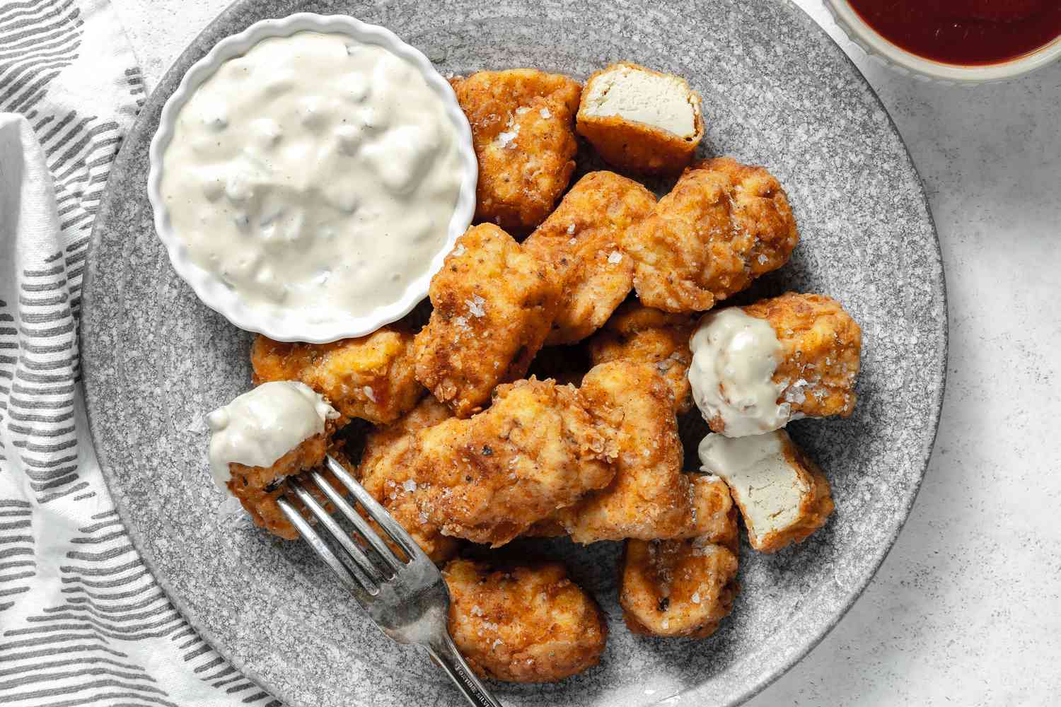 Vegan Chicken Nuggets Sprinkled with Salt Flakes on a Plate with a Bowl of Sauce, and Next to Plate, Another Bowl of Sauce and a Table Napkin