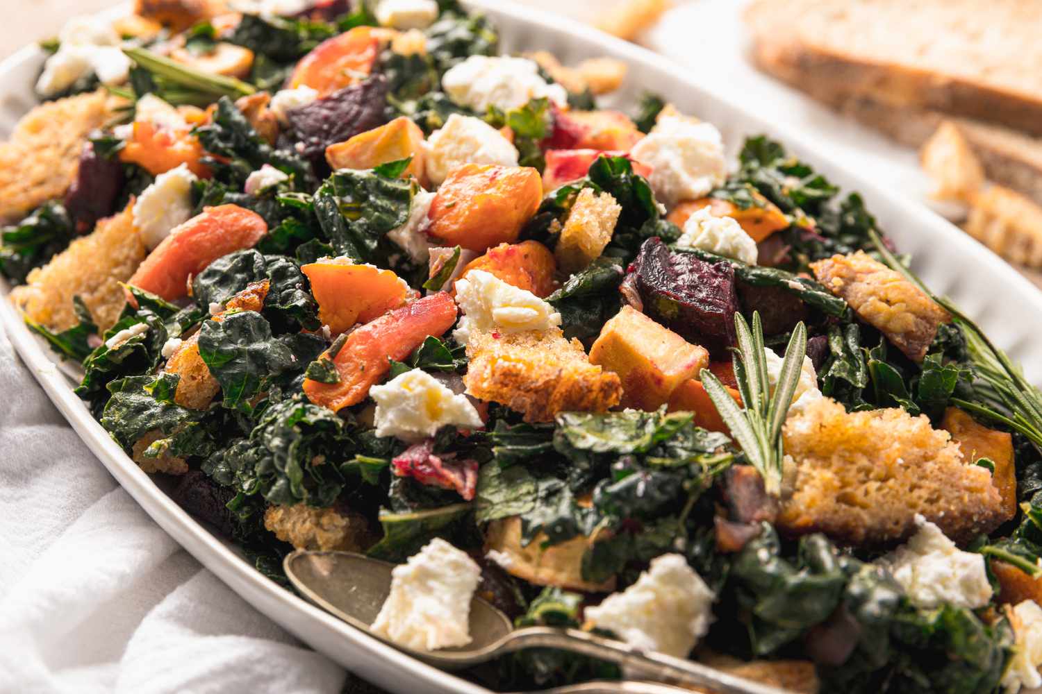 Platter of Roasted Root Vegetable Panzanella with a Serving Spoon, Sitting on a Kitchen Linen Next to Slices of Bread