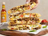 Hand Removing a Wrap from a Stack of Copycat Crunchwrap Supreme Wraps Cut in Half on Parchment Paper Over a Wooden Board