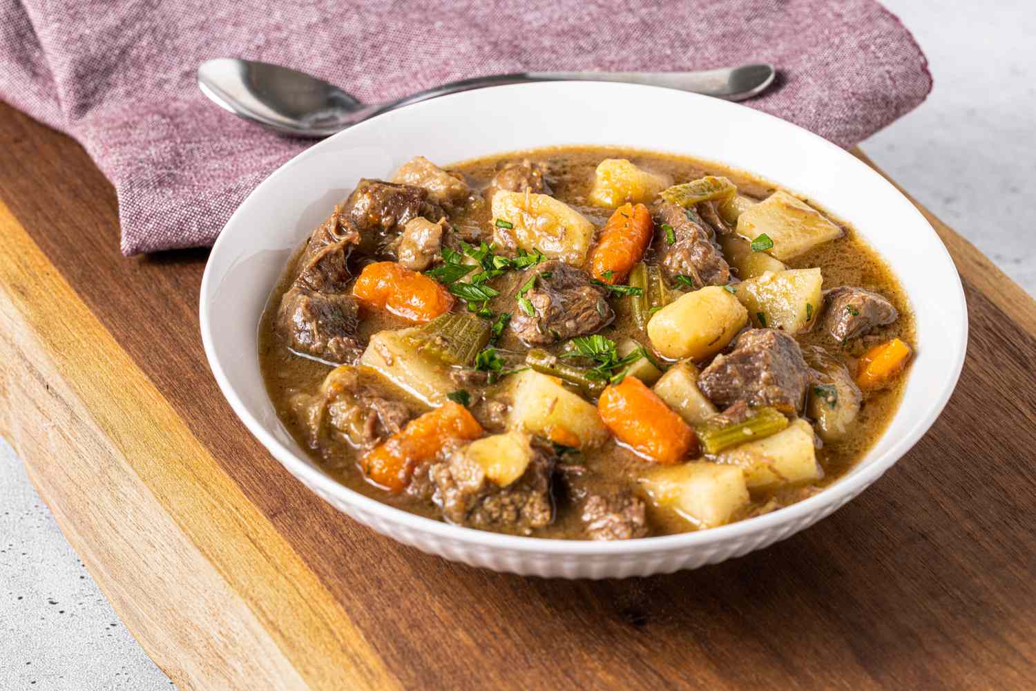 Bol de ragoût de bœuf facile garni de persil, avec en arrière-plan un torchon de cuisine et une cuillère dessus