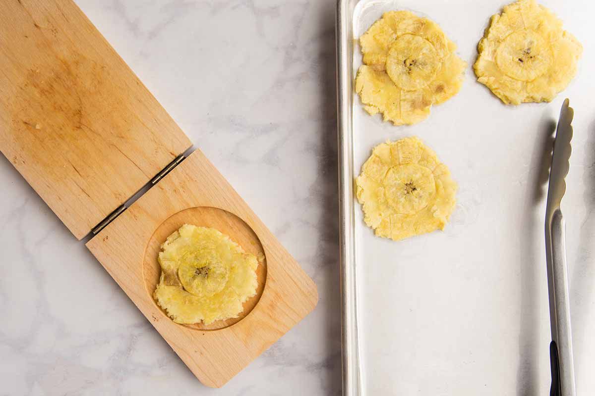 Écraser les plantains dans une tostonera et les déposer sur une plaque de cuisson tapissée de papier sulfurisé.