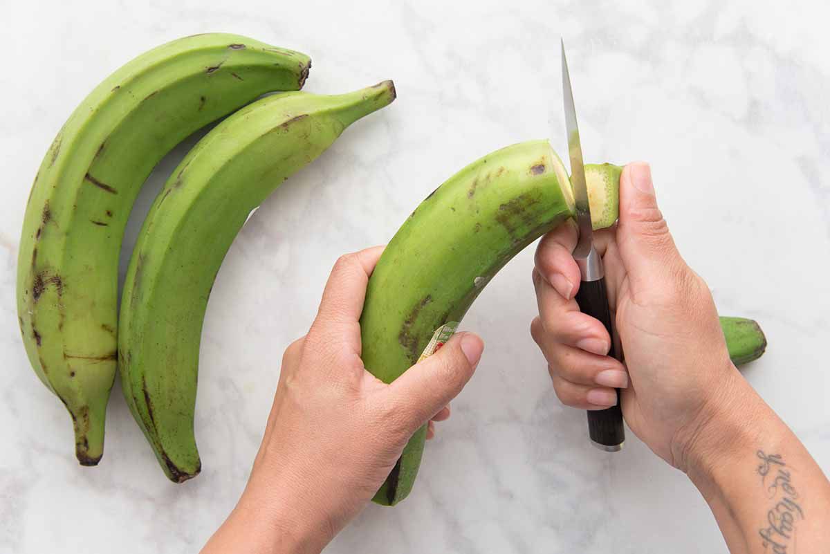 Personne coupant le haut d'une banane plantain verte.