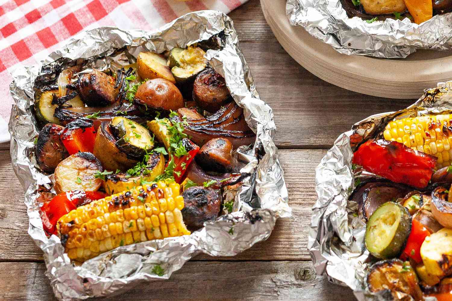 Packs de papier d'aluminium avec saucisse, maïs, courgette et pommes de terre et un tissu à carreaux rouge