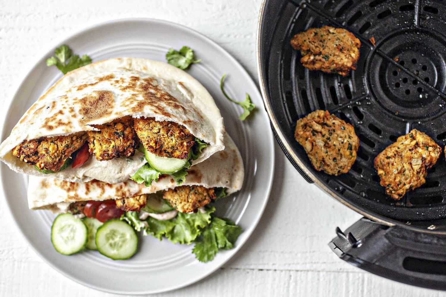 Une assiette de falafel dans un pita à côté d'une friteuse à air avec plus de falafel