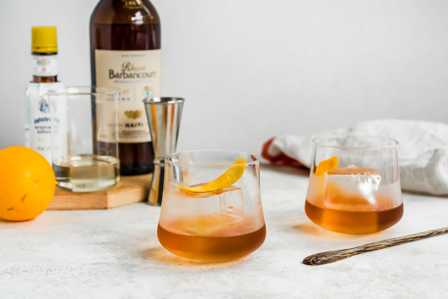 Glasses of Rum Old Fashioned with an Orange Peel with Ingredients and Supplies in the Background